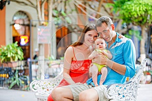 Happy family sitting on a bench with their cute baby girl