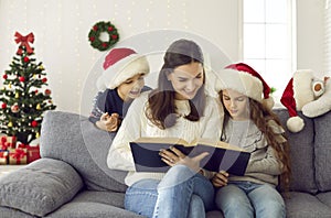 Happy family sitting on couch in decorated living room and reading book of Christmas stories