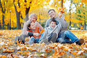 Happy family sitting on fallen leaves, playing and having fun in autumn city park. Children and parents together having a nice day