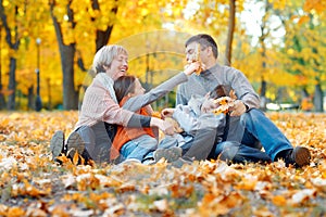 Happy family sitting on fallen leaves, playing and having fun in autumn city park. Children and parents together having a nice day