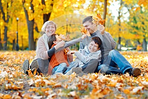 Happy family sitting on fallen leaves, playing and having fun in autumn city park. Children and parents together having a nice day