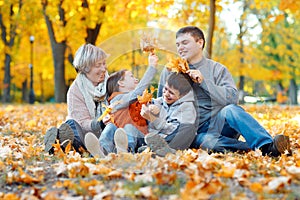 Happy family sitting on fallen leaves, playing and having fun in autumn city park. Children and parents together having a nice day