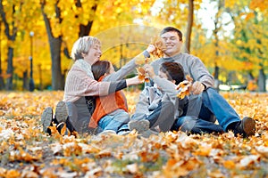 Happy family sitting on fallen leaves, playing and having fun in autumn city park. Children and parents together having a nice day