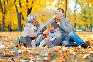 Happy family sitting on fallen leaves, playing and having fun in autumn city park. Children and parents together having a nice day