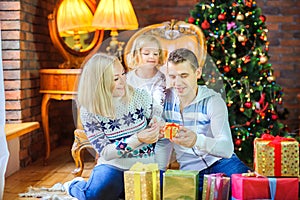 Family sitting on the floor near the Christmas tree congratulates and gives each other gifts