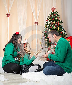 Happy family sitting in front a christmas tree and father gives a gift to his daughter