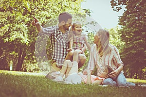 Happy family sitting on grass in the meadow together and enjoying in summer day.