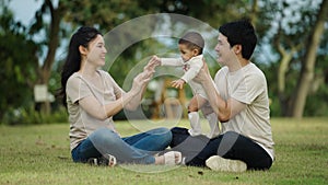 happy family sitting on a grass in park. father and mother talking and playing with infant baby.