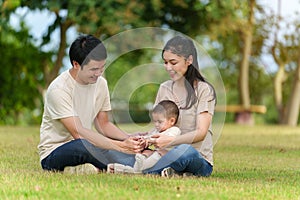 happy family sitting on a grass in park. father and mother talking and playing with infant baby