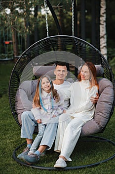 A happy family is sitting in a hammock on the lawn near the house