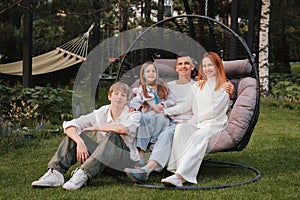 A happy family is sitting in a hammock on the lawn near the house