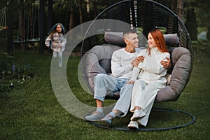 A happy family is sitting in a hammock on the lawn near the house