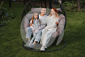 A happy family is sitting in a hammock on the lawn near the house