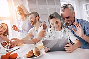 The happy family sitting with a laptop and the tablet at the table.