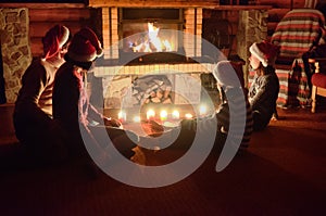 Happy family sitting near fireplace and celebrating Christmas and New Year, parents and children in Santa hats