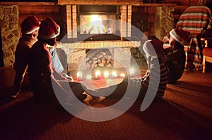 Happy family sitting near fireplace and celebrating Christmas and New Year, parents and children in Santa hats