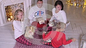 Happy family sitting near fireplace and gifting Christmas presents at holiday ev