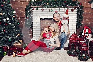 Happy family sitting near fireplace with little son and cute dog and smiling.