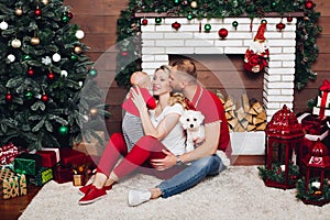 Happy family sitting near fireplace with little son and cute dog and smiling.