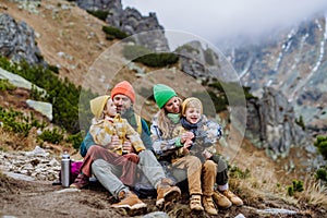Šťastná rodina sedí a odpočívá, během společné turistiky v podzimních horách.