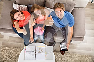 Happy Family Sitting On Sofa Gesturing Thumbs Up