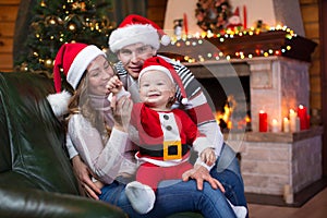 Happy family sitting on sofa near Christmas tree and fireplace in living room