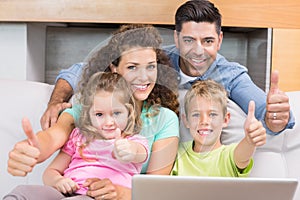 Happy family sitting on sofa using laptop giving thumbs up