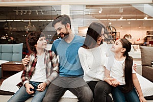 Happy family sitting on soft mattress in orthopedic furniture store. Healthy posture concept.