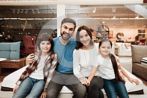 Happy family sitting on soft mattress in orthopedic furniture store. Healthy posture concept.