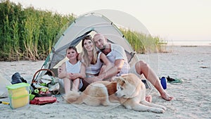 Happy family sitting in the tent on the beach with Akita Inu