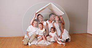 Happy family sitting under cardboard roof at home. Insurance concept