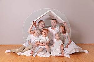 Happy family sitting under cardboard roof at home. Insurance concept