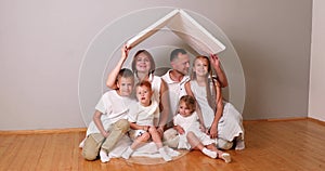 Happy family sitting under cardboard roof at home. Insurance concept