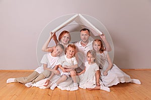 Happy family sitting under cardboard roof at home. Insurance concept