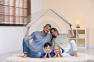 Happy family sitting under cardboard roof. Insurance concept
