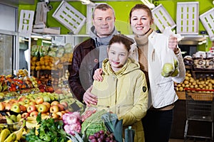 Happy family with small daughter standing with full grocery cart