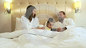 Happy family with smartphone in bed hotel room.