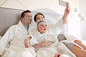 Happy family with smartphone in bed at hotel room