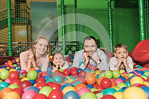 happy family smiling at camera while lying in pool with colorful balls