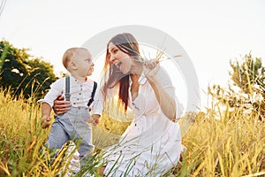 Happy family smiling and having fun. Young mother with her little son is outdoors in the agricultural field. Beautiful sunshine