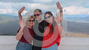 Happy family smiling and waving to camera against beautiful Mountain View. Tourists posing in front of valley and