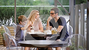 Happy family with son spending time together in outdoor terrace. Wife and husband talking while boy eating dessert with
