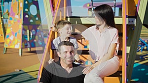 Happy family spending leisure time together in playground in summer day. Mather, father and son sitting on stairs of