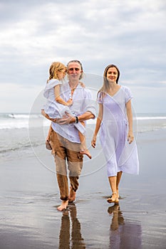 Happy family spending time at the beach. Summer holidays. Family vacation. Mother, father and daughter walking along the beach.