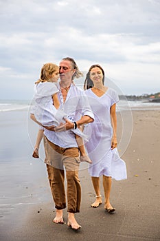 Happy family spending time at the beach. Summer holidays. Family vacation. Mother, father and daughter walking along the beach.