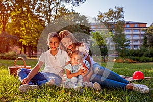 Happy family spending time outdoors sittting on grass in park. Mom with two children smiling. Mother`s day