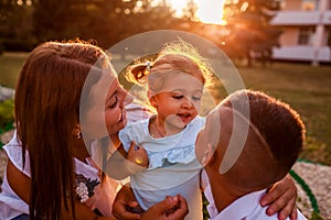 Happy family spending time outdoors walking in park. Mother and her son hugging little toddler girl and talking