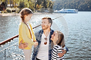 Happy family spending time together outside near lake. Parents playing with daughter hugging and having fun