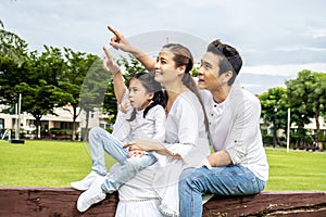 Happy family spending time together in the park, Beautiful asian family sitting on a chair in the park, pointing at something and