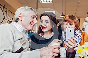 Happy family spending time together. Senoir family couple with adult daughter using a smartphone in the cafe.